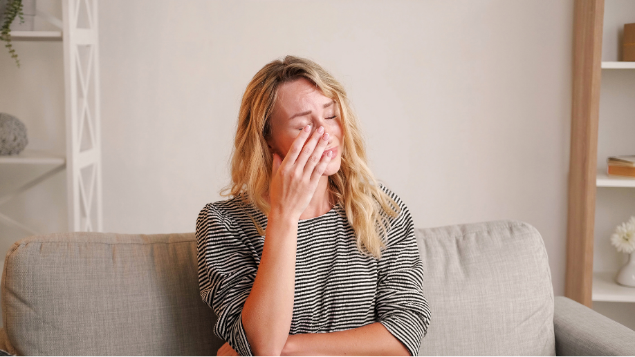 Jeune maman assise sur un canapé, en train de pleurer, exprimant des signes de dépression post-partum. Image illustrant les symptômes de la dépression post-partum, le besoin de soutien et les ressources pour trouver de l'aide. Elle veut garder le lien maternel malgré les difficultés émotionnelles.